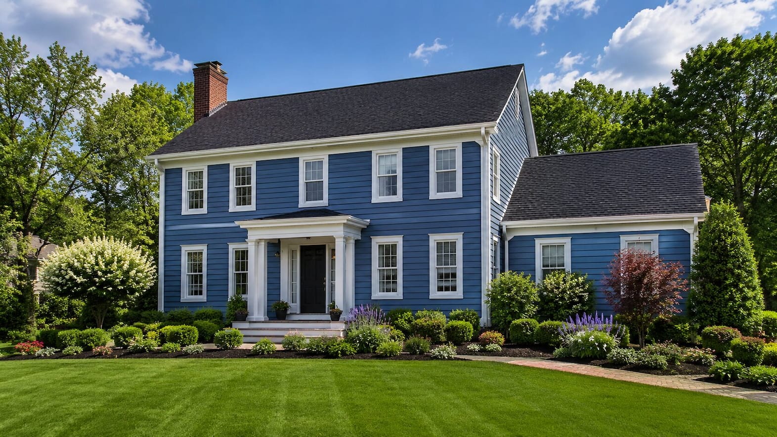 Dark blue colonial-style home with white trim and landscaped front yard.