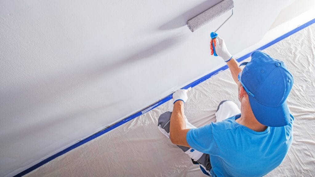 Painter in blue shirt rolling grey paint onto a wall