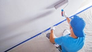 Painter in blue shirt rolling grey paint onto a wall