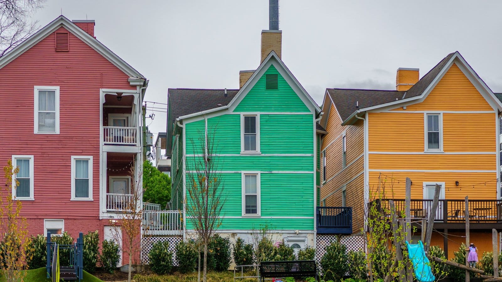 Brightly colored houses in a neighborhood on a cloudy day showcasing diverse exterior paint choices.